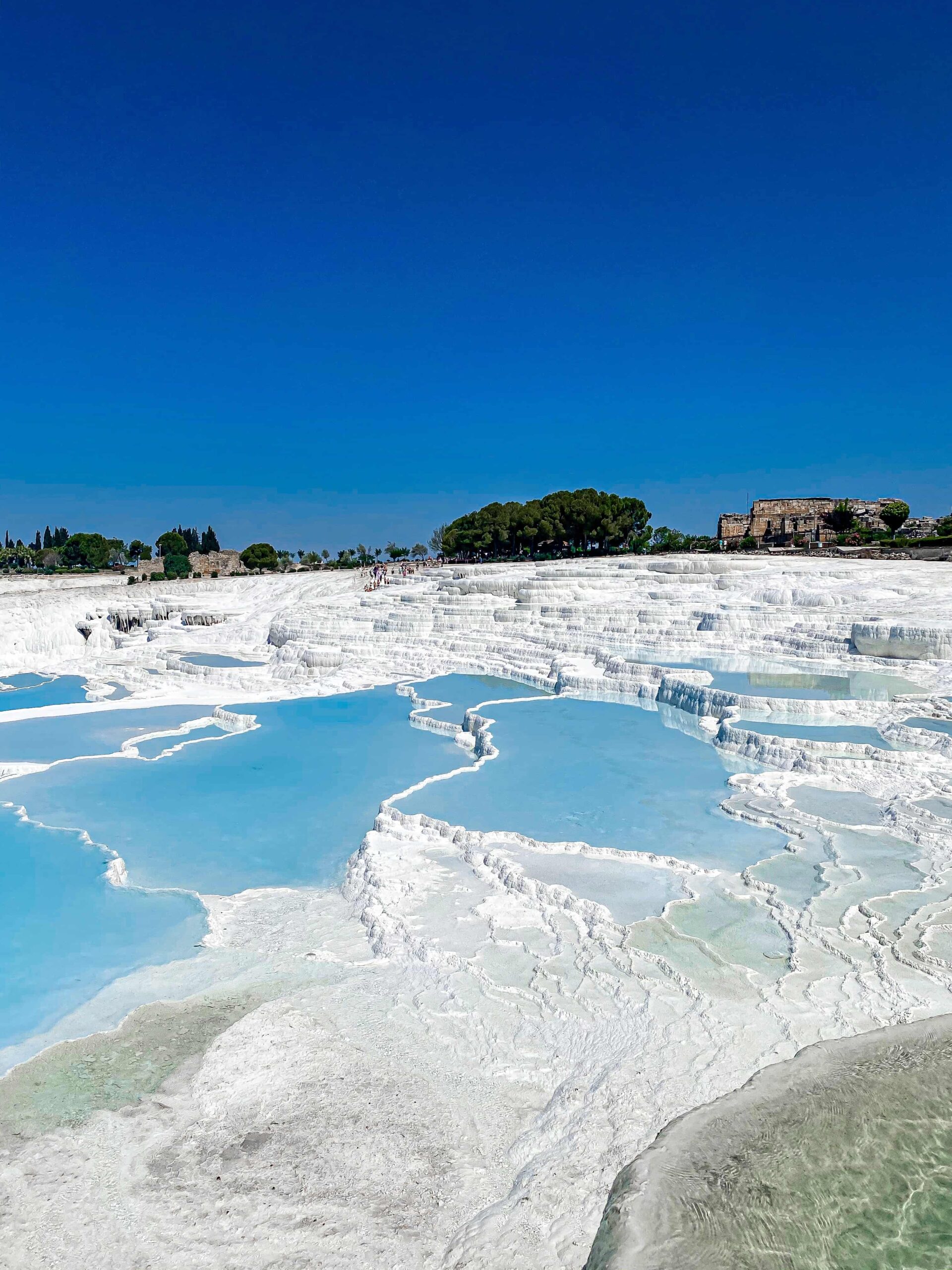 Pamukkale, meaning 'cotton castle' in Turkish, is a natural site known for the mineral-rich thermal waters flowing down white travertine terraces on a nearby hillside.