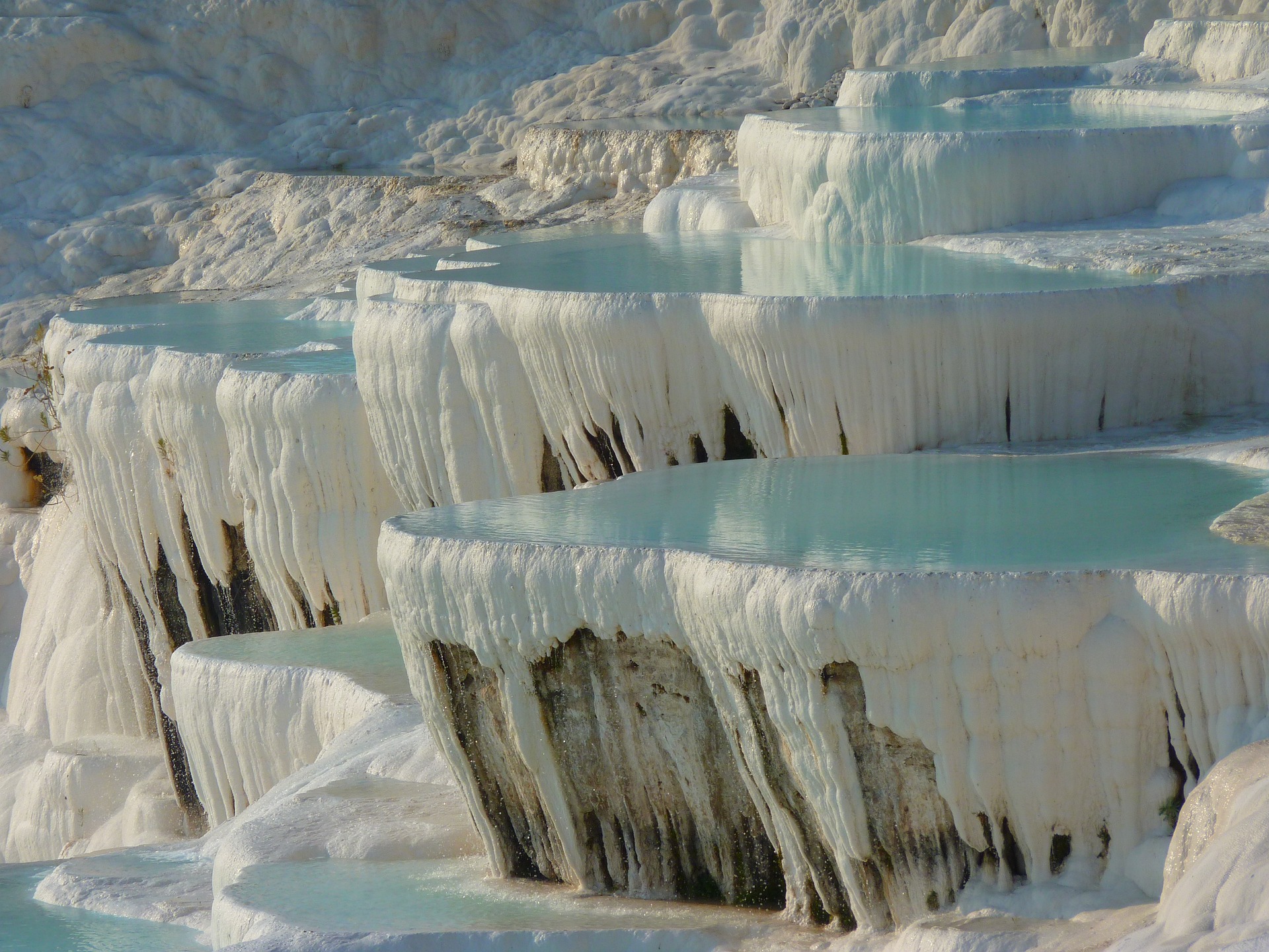 Pamukkale, meaning 'cotton castle' in Turkish, is a natural site known for the mineral-rich thermal waters flowing down white travertine terraces on a nearby hillside.